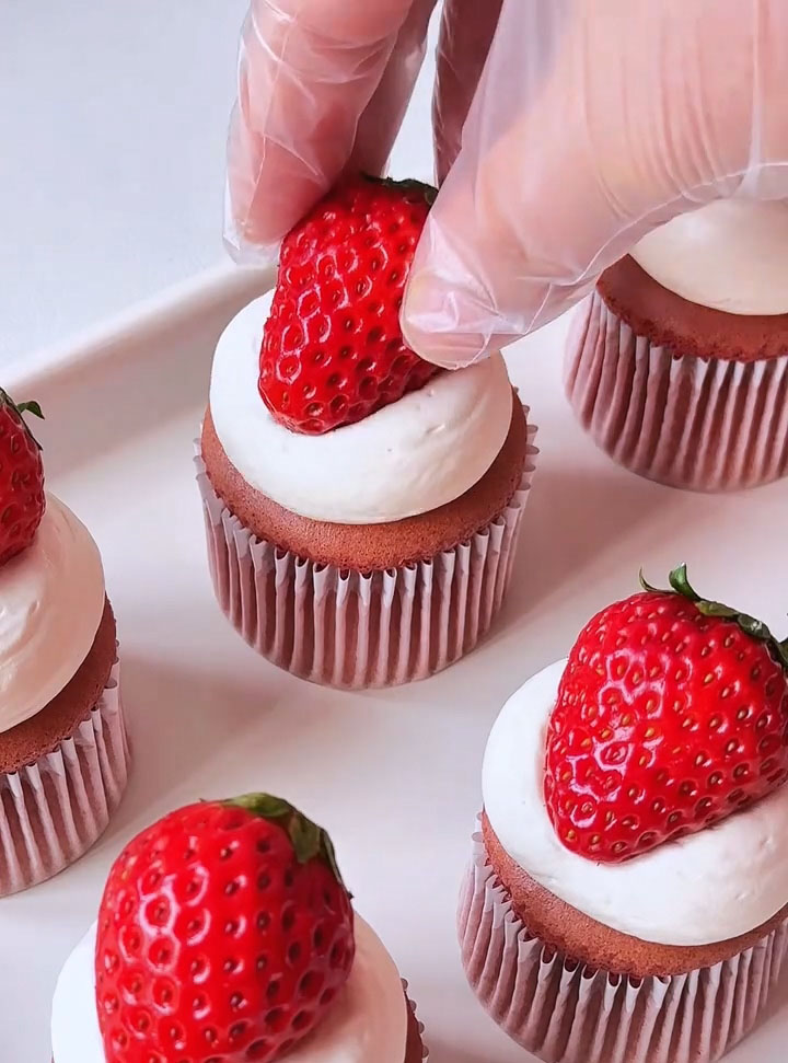 Place a fresh strawberry on top of the cream on each cupcake
