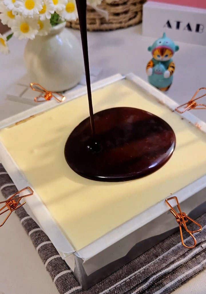 Slowly pour the cooled chocolate glaze over the set cheesecake layer