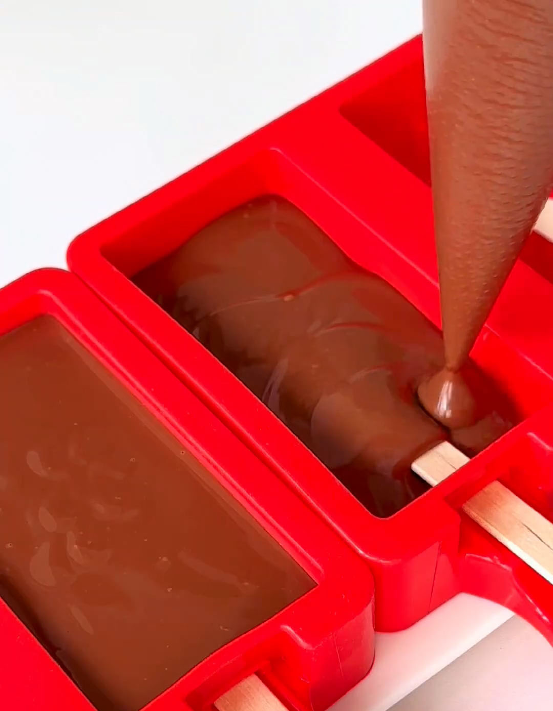 Carefully pipe or pour the warm chocolate mixture into your popsicle molds
