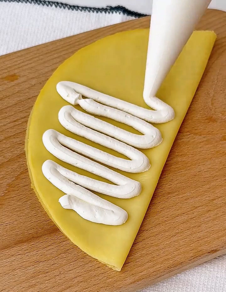 Spread a generous, even layer of whipped cream over the folded crepe